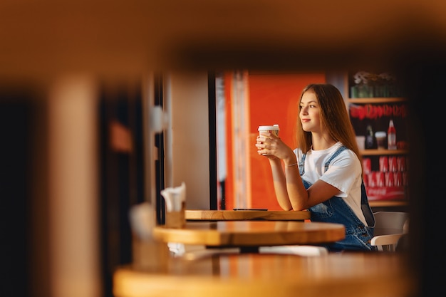 Молодая привлекательная милая девушка в кафе с кофе и телефон на лучах утра