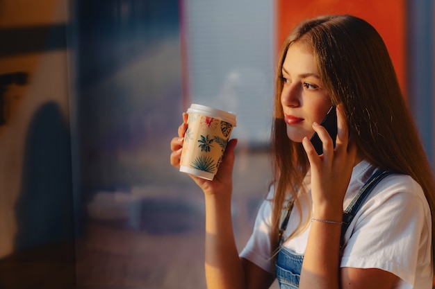 朝の梁でコーヒーと電話でカフェで若い魅力的なかわいい女の子