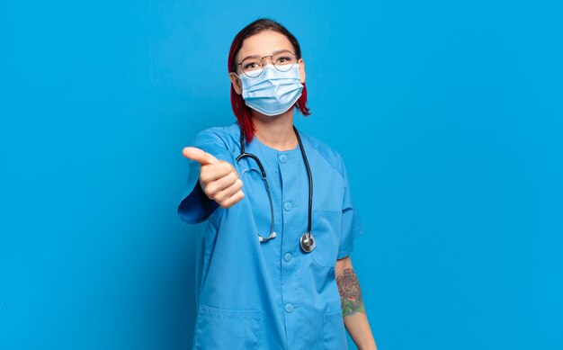 Young attractive red hair nurse feeling proud, carefree, confident and happy, smiling positively with thumbs up.