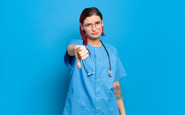 Young attractive red hair woman feeling cross, angry, annoyed, disappointed or displeased, showing thumbs down with a serious look. hospital nurse concept