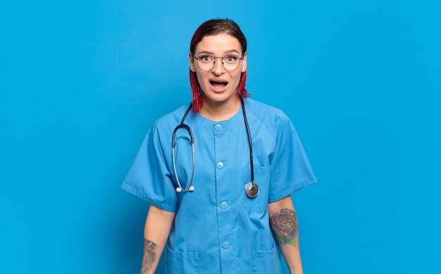 Young attractive red hair woman looking very shocked or surprised, staring with open mouth saying wow. hospital nurse concept