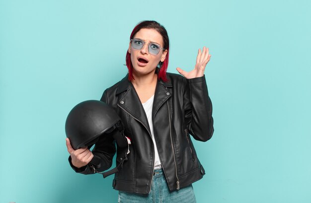 Young attractive red hair woman screaming with hands up in the air, feeling furious, frustrated, stressed and upset.