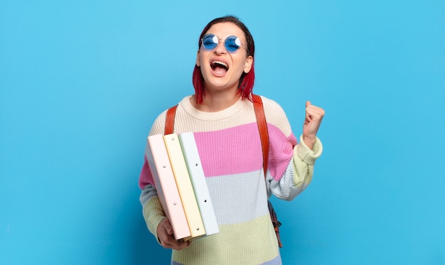 Young attractive red hair woman shouting aggressively with an angry expression or with fists clenched celebrating success