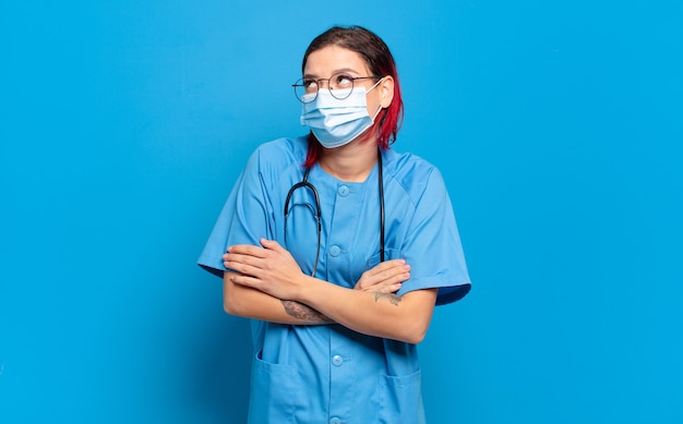 Young attractive red hair woman shrugging, feeling confused and uncertain, doubting with arms crossed and puzzled look. hospital nurse concept