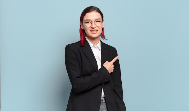 Young attractive red hair woman smiling cheerfully, feeling happy and pointing to the side and upwards, showing object in copy space