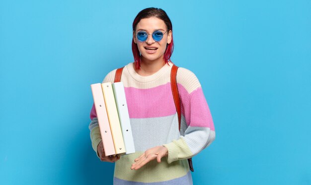 Young attractive red hair woman smiling cheerfully, feeling happy and showing a concept in copy space with palm of hand. university student concept