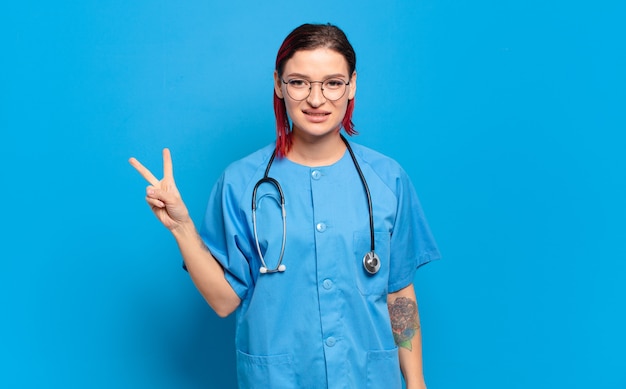 Young attractive red hair woman smiling and looking friendly, showing number two or second with hand forward, counting down. hospital nurse concept