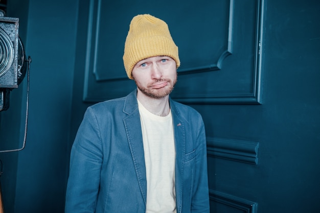 Young attractive sad man infantile loser hipster in the yellow hat on blue background