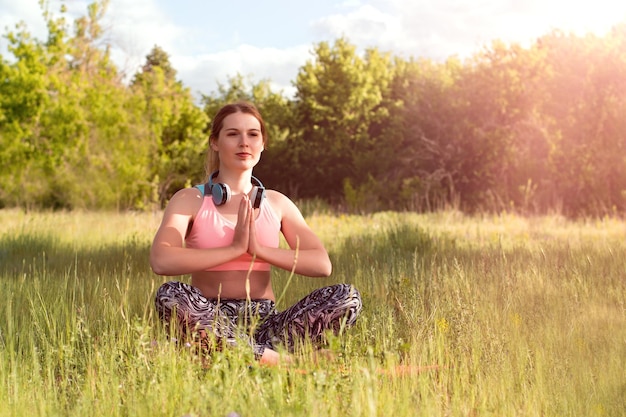 Young attractive slim woman in sport clothes doing yoga meditating in the park with pine trees in background Healthy lifestyle concept