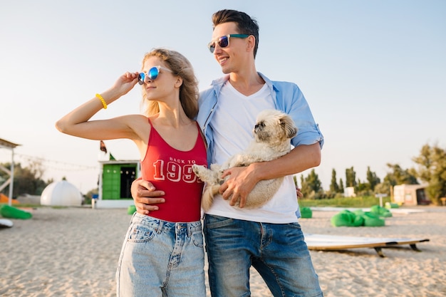 Young attractive smiling couple having fun on beach playing with dog