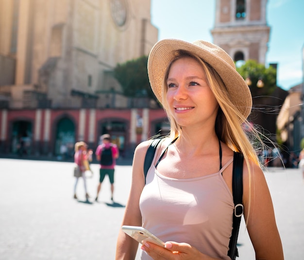 Young attractive smiling girl tourist in hat exploring new Europe city at summer holiday