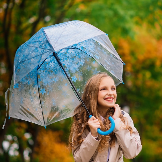 Young attractive smiling girl under umbrella in an autumn forest