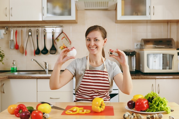 앞치마를 입은 젊고 매력적인 웃는 여성은 부엌에서 닭고기와 메추라기 알 중에서 선택합니다. 다이어트 개념입니다. 건강한 생활. 집에서 요리. 음식을 준비하다.