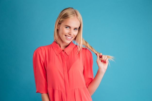 Young attractive smiling woman in red dress holding her strong hair isolated on a blue wall