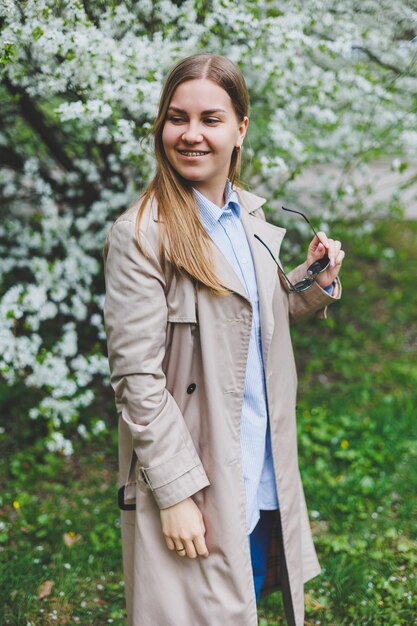 Young attractive smiling woman with a beautiful hairdo on a background of blooming pink apple tree Selective fokus in woman