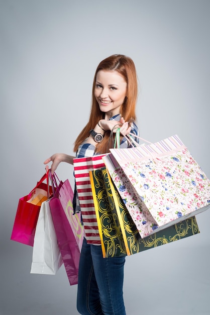 Young attractive smiling woman with many colored shopping bags on gray. Woman making shopping