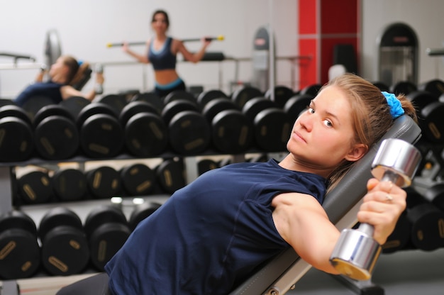 Молодая привлекательная спортивная девушка в спортивной одежде на фитнес-оборудовании, тренирующейся с гантелями в тренажерном зале