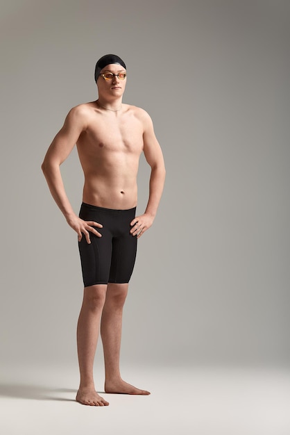 young attractive swimmer in excellent physical shape in purple swimming shorts, on a gray background, copy space.