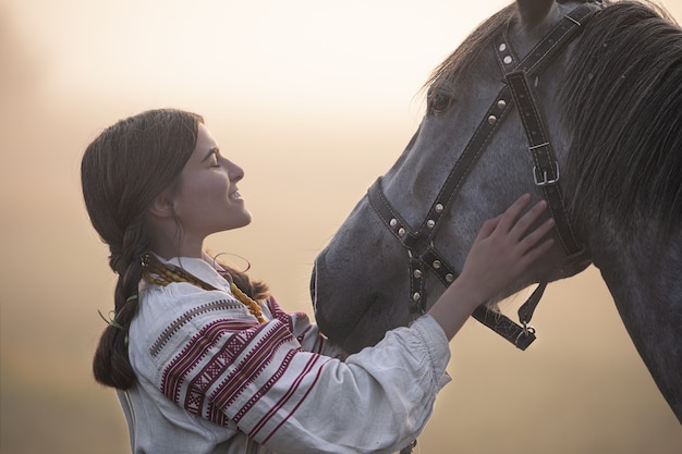 Young attractive white woman in noble clothes stroking a horse.