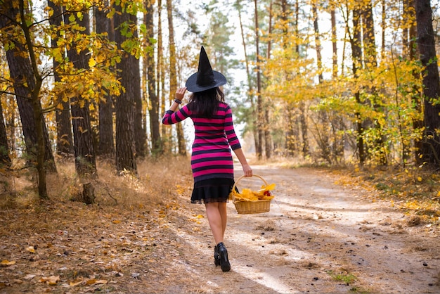 La giovane strega attraente cammina nel concetto di foresthelloween arancione autunnale