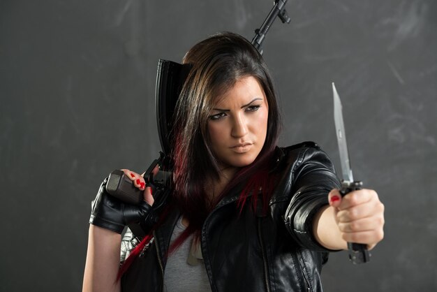 A young attractive woman armed with an automatic rifle and a knife standing with outstretched hand holding a knife.