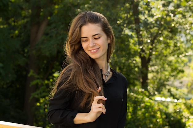 Young attractive woman in black blouse and silver necklace on the background of green trees