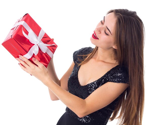 赤いプレゼントを保持し、白い背景でそれを見て黒いドレスの若い魅力的な女性