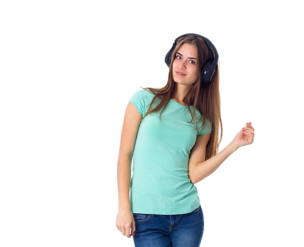 Young attractive woman in blue T-shirt and jeans  in black headphones on white background in studio