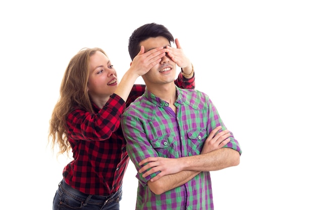 Young attractive woman closing eyes of young pleasant man with dark hair in plaid shirt