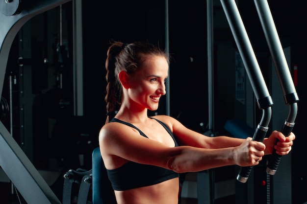 Young attractive woman doing exercises for arms in a training machine