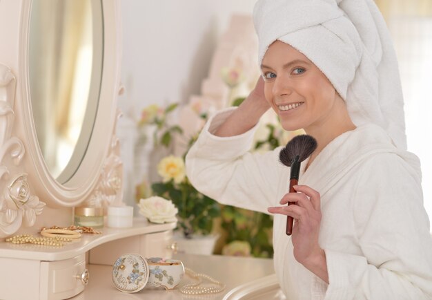 Young attractive woman doing make up after shower at boudoir