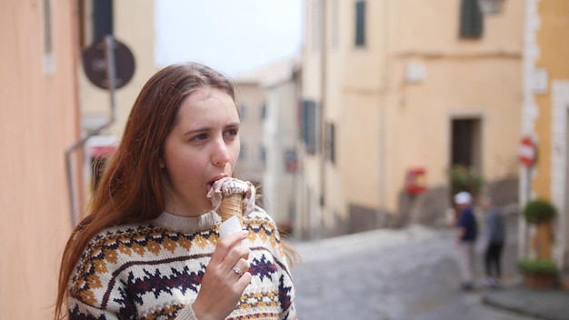 사진 젊은 매력적인 여자는 역사적인 마을의 좁은 거리에서 아이스크림을 먹는다