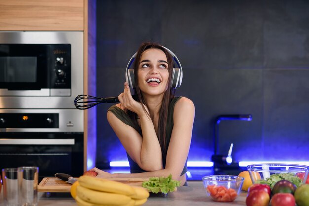 Young attractive woman eats red apple and listens to the music at kitchen in morning. Healthy lifestyle concept, enjoying breakfast.