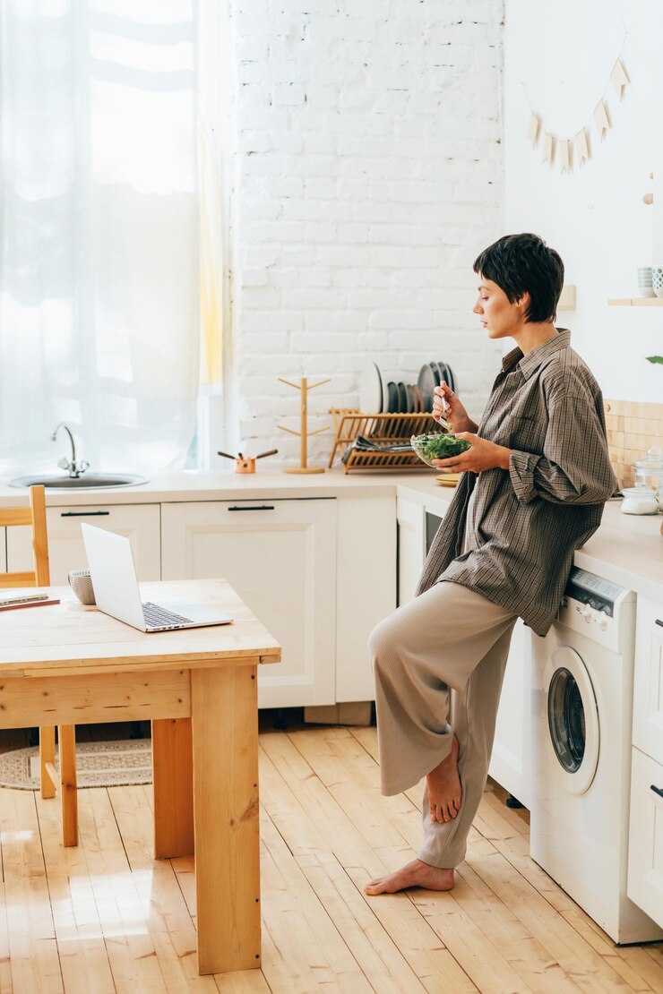 Photo キッチンに立ってラップトップでビデオを見ながらサラダを食べている魅力的な若い女性