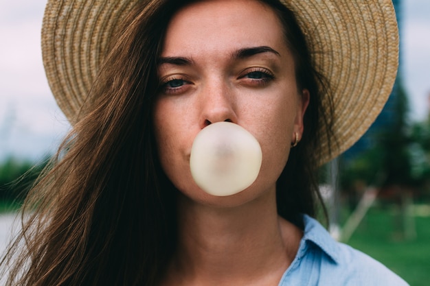 Young attractive woman in hat blowing bubble of chewing gum on the street