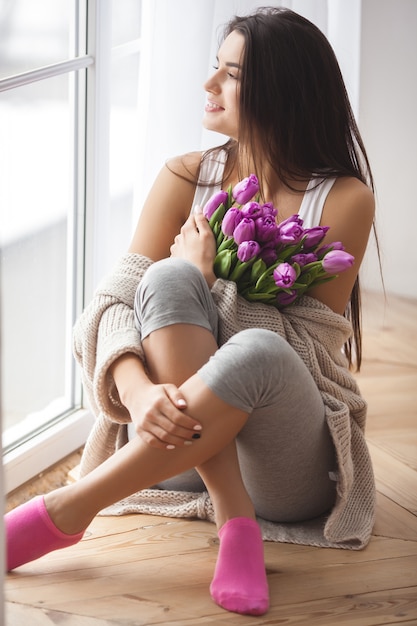 Photo young attractive woman holding flowers. beautiful lady with tulips liying on the bed