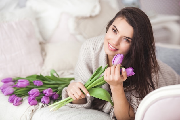 Молодая привлекательная женщина, держа цветы. красивая дама с тюльпанами лежит на кровати