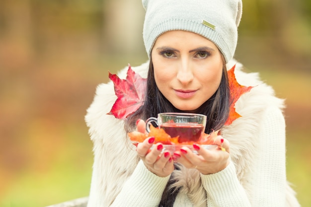 Young attractive woman holding in hand hot red tea. Relaxing in autumn nature with hot tea.