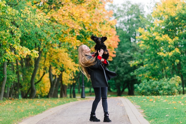 Young attractive woman holding her dachshund dog in her arms outdoors in sunrise in park at autumn time