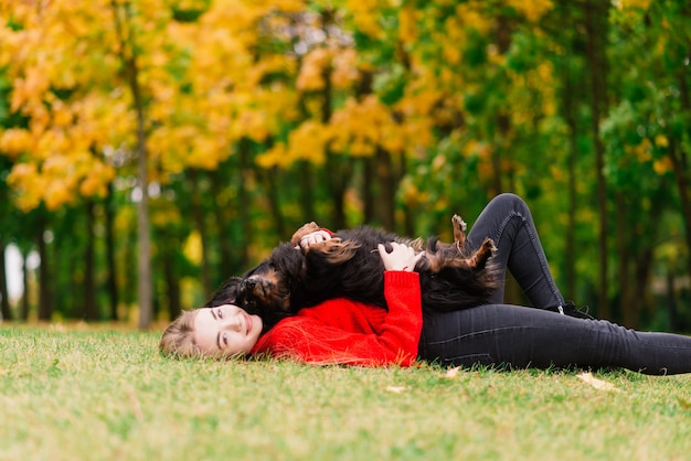 Young attractive woman holding her dachshund dog in her arms outdoors in sunrise in park at autumn time