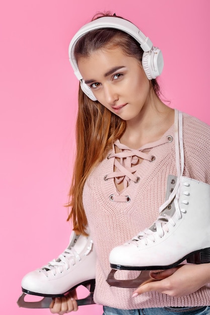 Young attractive woman holding ice skates on pink background