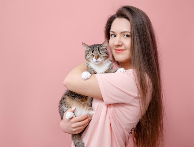 手で猫を抱き締める若い魅力的な女性、ピンクの背景