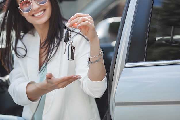 Молодая привлекательная женщина только что купила новую машину. женщина держит ключи от нового автомобиля.