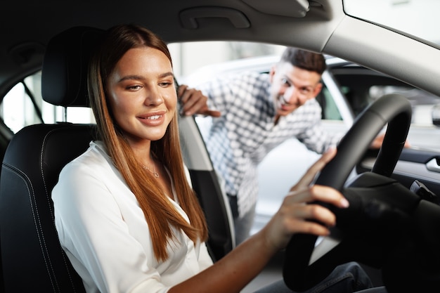 Young attractive woman looking for a new car in a car showroom