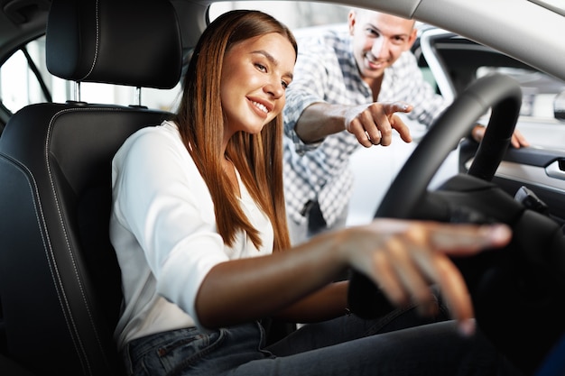 Young attractive woman looking for a new car in a car showroom