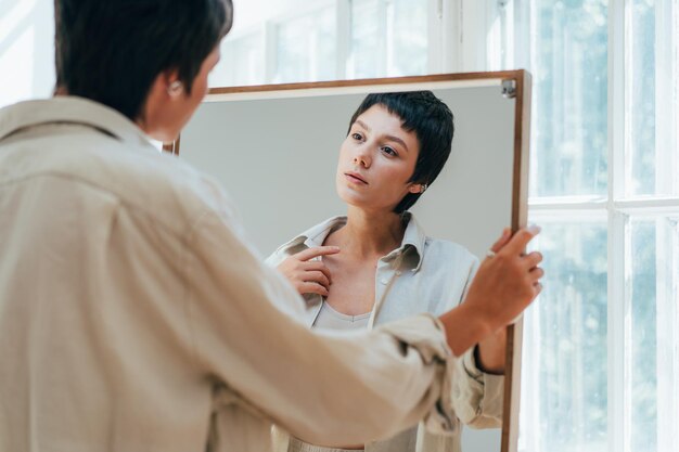 Photo a young attractive woman looks at her reflection in the mirror
