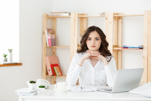 ノートパソコンでの作業と何かを考えて、近代的なオフィスの机で若い魅力的な女性。