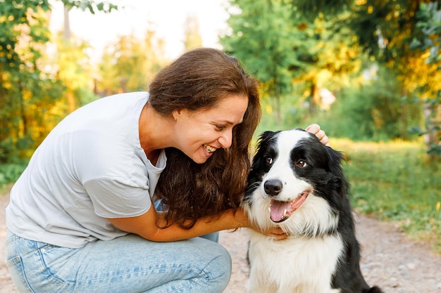 Young attractive woman playing with cute puppy dog border collie on summer outdoor background Girl kissing holding embracing hugging dog friend Pet care and animals concept