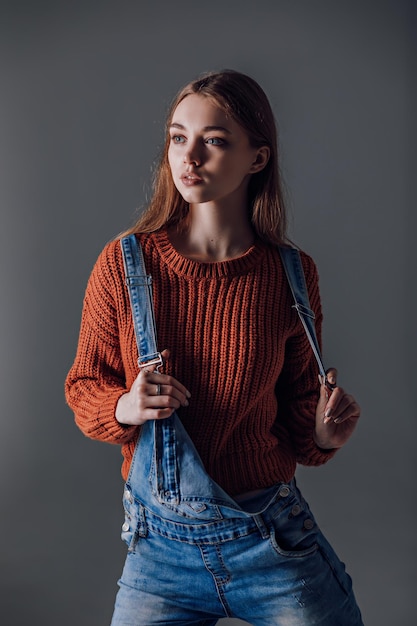 Молодая привлекательная женщина в красном свитере на сером фоне