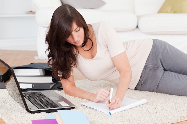 Young attractive woman relaxing with her laptop while writing on a notebook